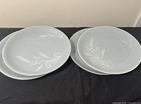 Four grey wheat pattern plates on black cloth