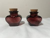Front view of two burgundy heart-shaped glass jars with corks