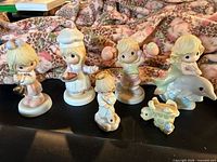 Front view of six of the seven Precious Moments figurines including watering can girl, baker girl, child with ball, dolphin rider, kneeling angel, turtle