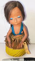 Front view of vinyl Hawaiian hula girl doll on yellow striped base showing outfit, tag and condition