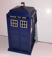 Front and side view of blue plastic Doctor Who TARDIS toy display with marker for scale