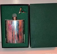 Hip flask and funnel seated in green presentation box with lid removed