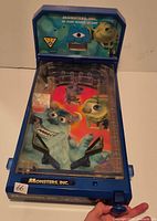 Front perspective of blue Monsters Inc tabletop pinball game showing playfield, flippers, plunger and backboard graphics