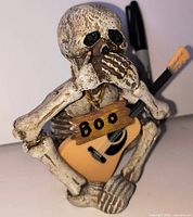 Front view of seated skeleton figurine holding guitar with Boo sign