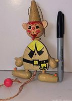 Front view of wooden Jumping Jack elf puppet beside marker for scale