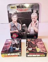 Front view of metal tin and two boxed card decks displaying AMC The Walking Dead branding