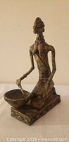 Full view of bronze kneeling woman sculpture with bowl and pestle