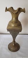 full view of brass vase standing upright showing ruffled rim, engraved body, pedestal base