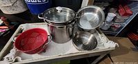 Overview of stock pot, lid, red colander, steamer baskets and perforated pan