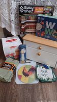 Full lot overview showing boxed Spicy Shelf, WW Healthy Kitchen set, Rubbermaid storage set, towels, trivet, pot holder, cutting board and small wooden cabinet