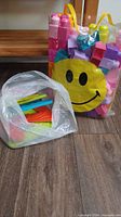 Two clear plastic bags, one smiley face bag filled with foam letters, another bag filled with plastic blocks