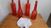 four red glass bottles with corks and white crocheted doily on wooden surface