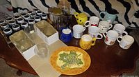 Wide view showing mugs, spice tins in holders, glass jars, ceramic plate and stoneware pieces on table