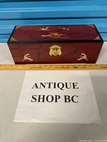 Front view of entire red lacquered box showing brass clasp, crane motifs and overall size