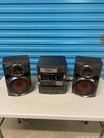 Front view of JVC MX-D401T receiver flanked by two Panasonic SB-AK220 speakers