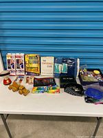 Wide view of all items on table including books, spoons, lantern, cameras, tin, craft bags