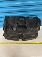Full view of black leather rolling duffel with tape measure showing width, front pockets visible