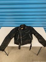Full view of black leather motorcycle jacket laid flat on table showing overall style and condition