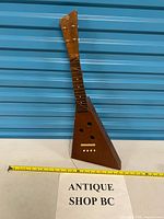 Full view of triangular wooden folk instrument with tape measure for scale