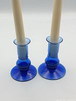 Front view of both cobalt blue glass candlestick holders with candles inserted