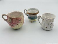 Front view of three small decorative porcelain cups showing colors, patterns, and gilt accents
