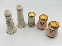 Front view of all five shakers highlighting shapes, floral designs and gold tops