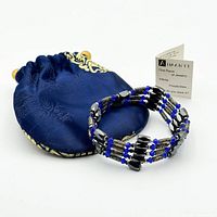 Bracelet coiled beside navy satin pouch and info card