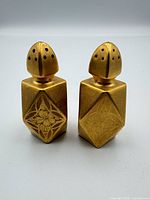 Front view of both gold faceted shakers showing floral engravings and gilt finish