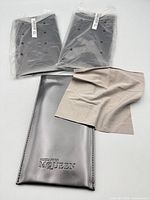 Two factory-sealed metallic gunmetal pouches and one unwrapped with beige microfiber cloth on top