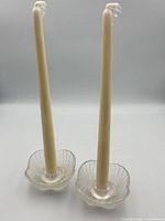 Two ivory taper candles standing in clear/frosted pressed glass flower-form holders