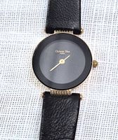 Front view showing black dial, gold bezel, hands and leather strap