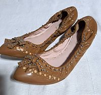 Three-quarter view of both shoes showing leather, studs, bow, and overall condition