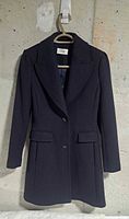 Front view of navy Reiss coat on hanger against wall