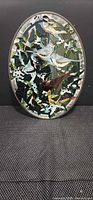 Front view of entire oval stained glass panel in metal frame showing bird and foliage design