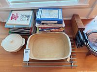 Overview showing rectangular casserole on trivet, knife block with knives, stack of cookbooks, round lidded dish partially visible