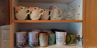 Cabinet shelf showing full assortment of mugs, glass creamer and sugar bowl