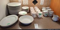 Stacked dinner plates, salad plates, bowls, cups and creamers displayed on countertop