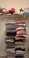 Overall view of hats on wire shelf and folded garments on rack