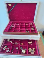 Open jewelry box showing upper tray compartments with assorted small jewelry and lower drawer with larger pieces