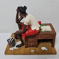 Front left view of figurine showing seated woman on desk with accessories