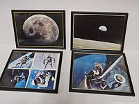 Four framed NASA prints laid flat showing lunar surface, Earthrise, spacewalk collage and docking scene