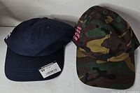 Both caps front view showing navy cap with tag and camo cap with embroidery