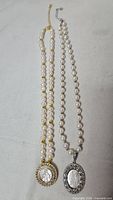 Both pearl necklaces laid out showing pendants and strands