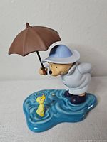 Front view of Pooh figurine holding umbrella, duck on blue puddle base