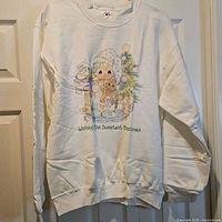 Full front view of white Precious Moments Christmas sweatshirt on hanger