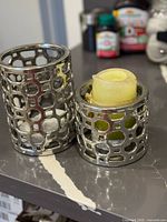 Two silver-tone lattice cylindrical candle holders on countertop