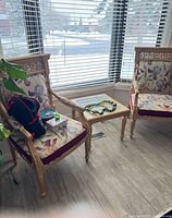 Two carved wood armchairs with floral upholstery and matching glass-top side table