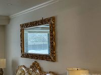 Rectangular mirror with ornate gold carved frame hung on wall
