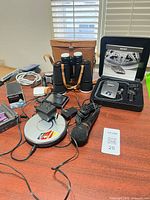 All items arranged on tabletop showing Walkman, binoculars with case, Passport 8500 radar detector set, microphone, radio, adapters and cables