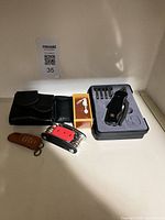 Group shot of all items including black multi-tool, bit holder, red multi-tool, leather pouch, fob and orange box